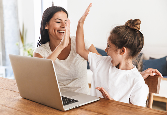 Mother and young daughter high-fiving at their laptop