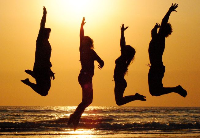 Four friends in silhouette jumping for joy on beach at sunset