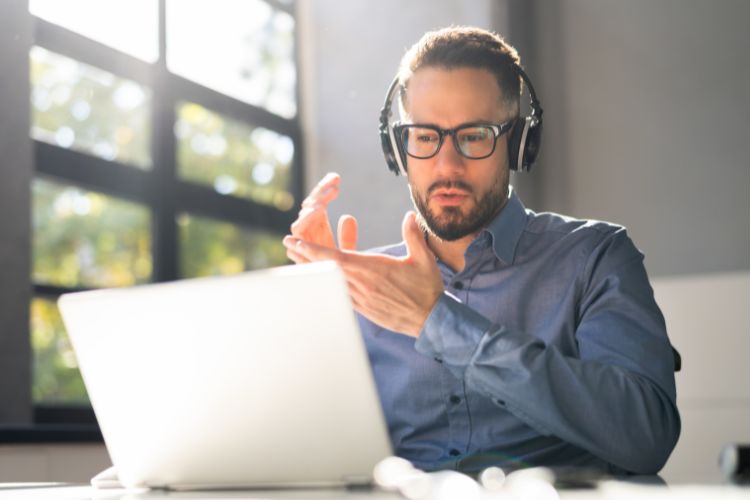 Photo of man at laptop with headphones listening to screen